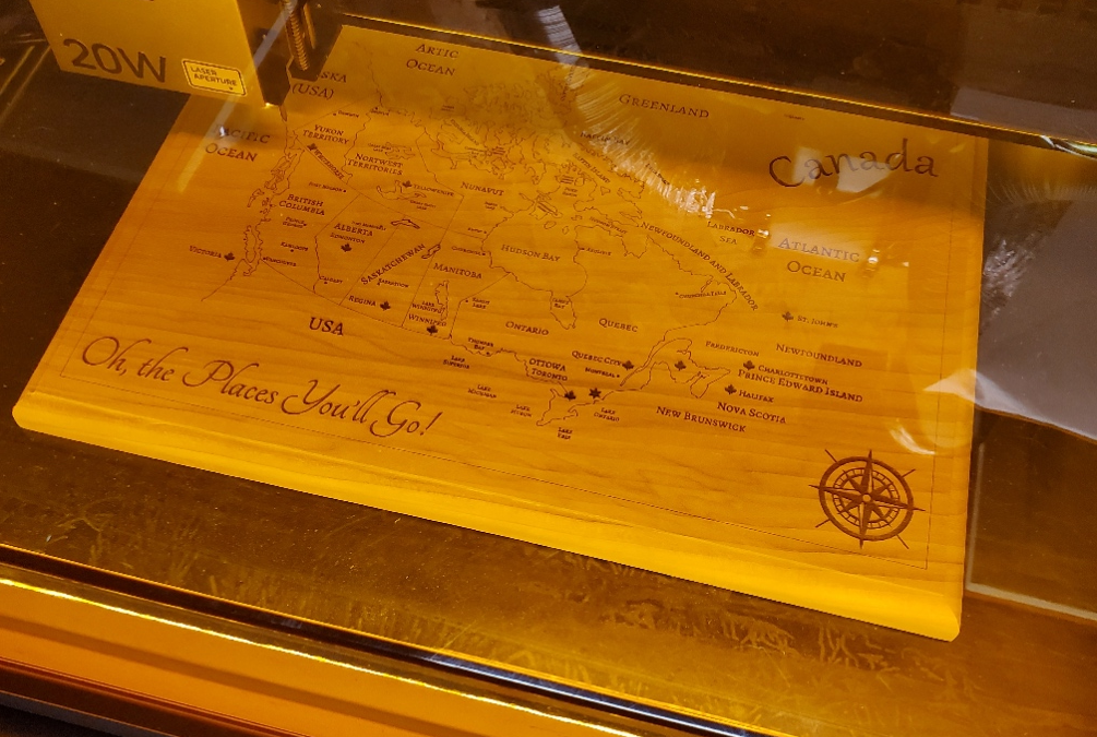 A laser bed engraving a Canadian map in a piece of poplar